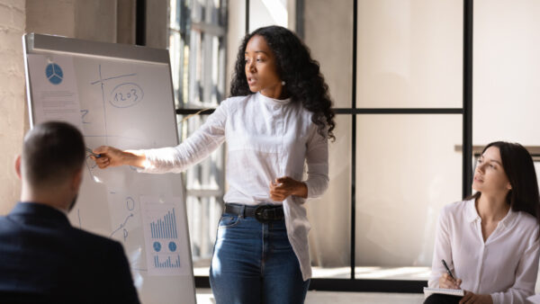 Three colleagues sit as part of an office presentation with whiteboard full of charts