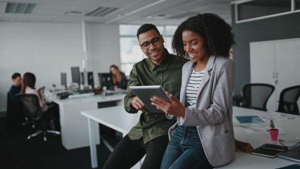 Two people in an office smiling working on a tablet