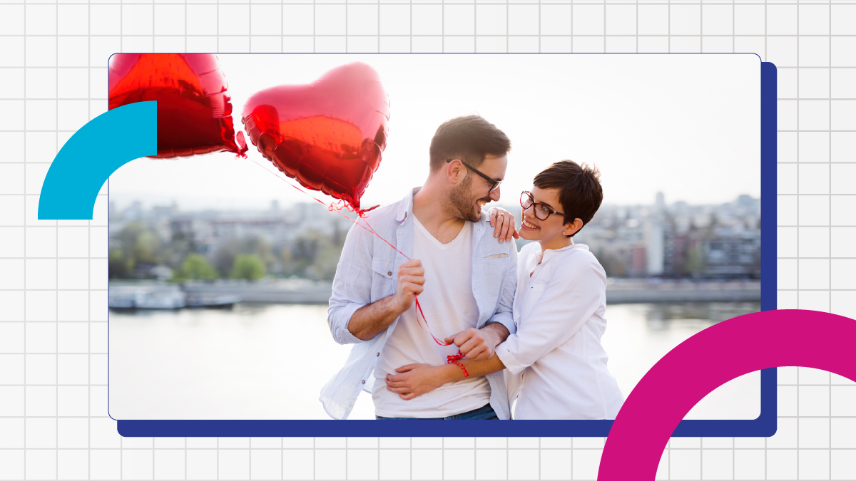 Couple stand on a bridge with two red foil heart shaped ballons